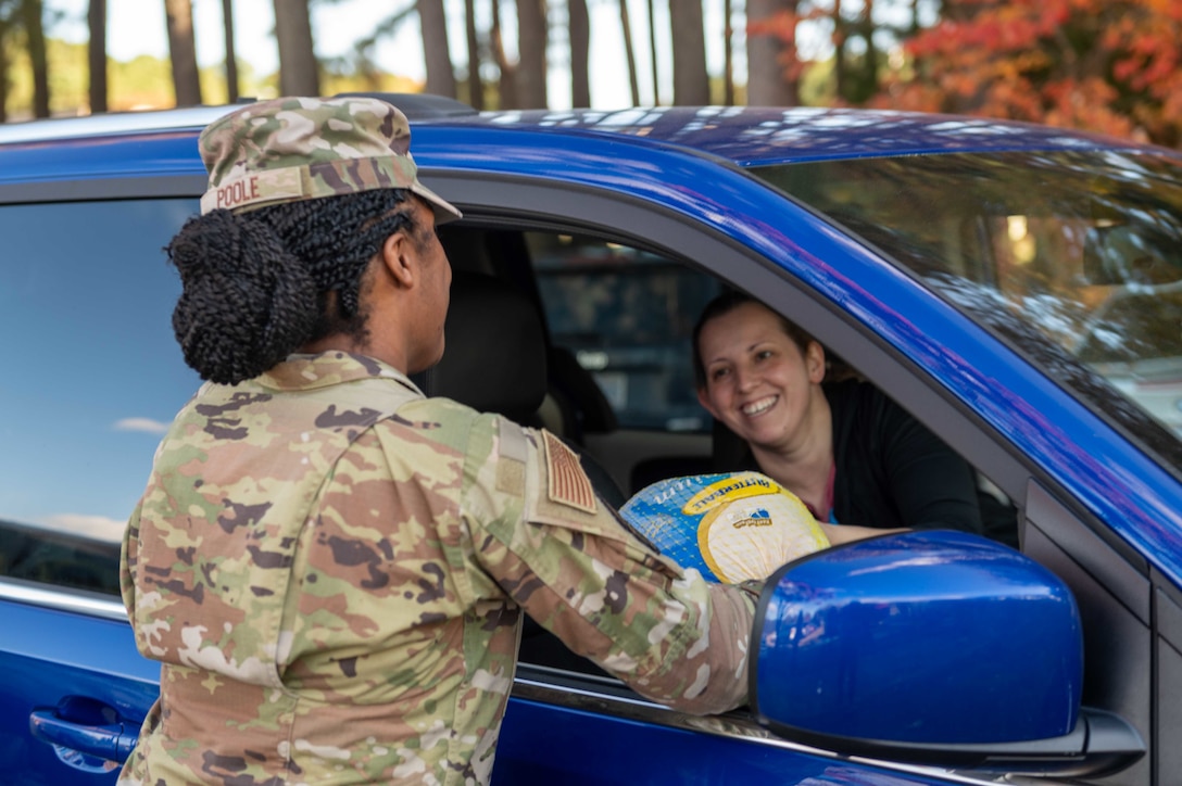 An airman hands a turkey to another in a car.
