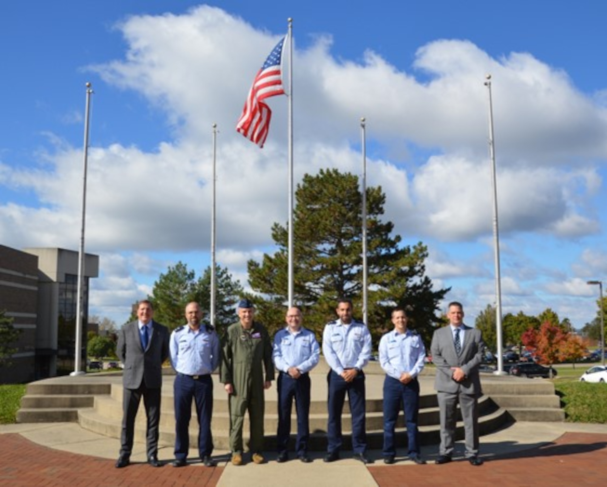 Seven men stand outdoors in front of the American flag.
