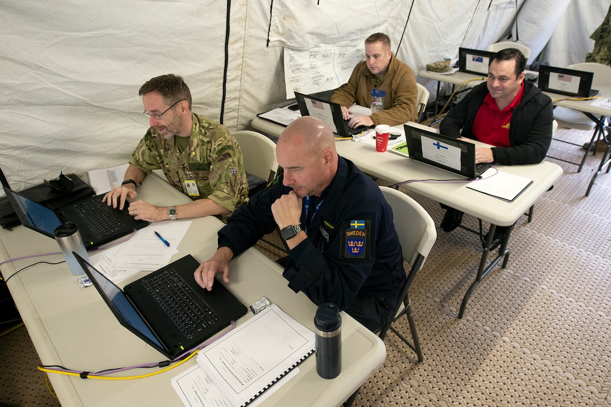 Men sit at tables in front of laptop computers.