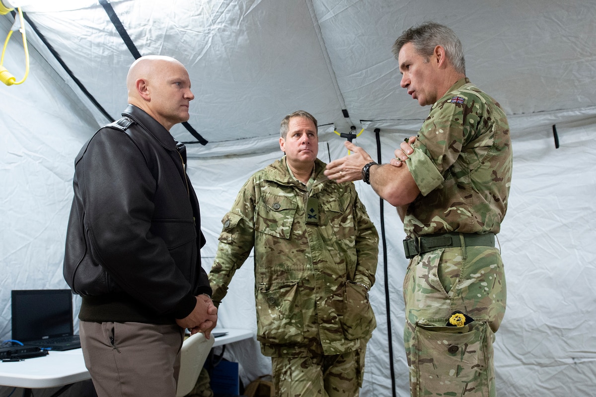 Three men talk to one another.