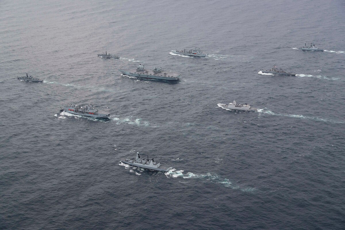 Multiple military ships move together in the ocean.