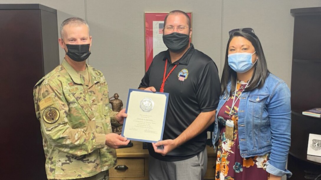 Col. Jason Kalin poses  with Timothy Henning and his wife Heather to present him with a certificate marking his 20 years of federal service.