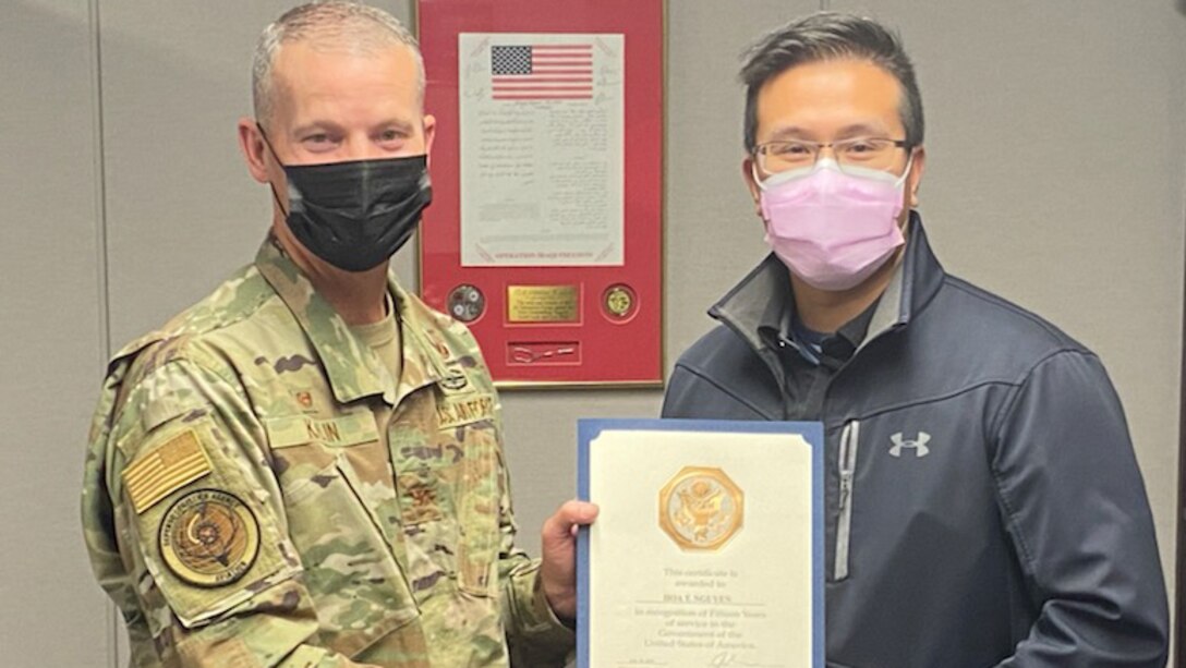 Col. Jason Kalin poses  with Tommy Nquyen to present him with a certificate marking his 15 years of federal service.