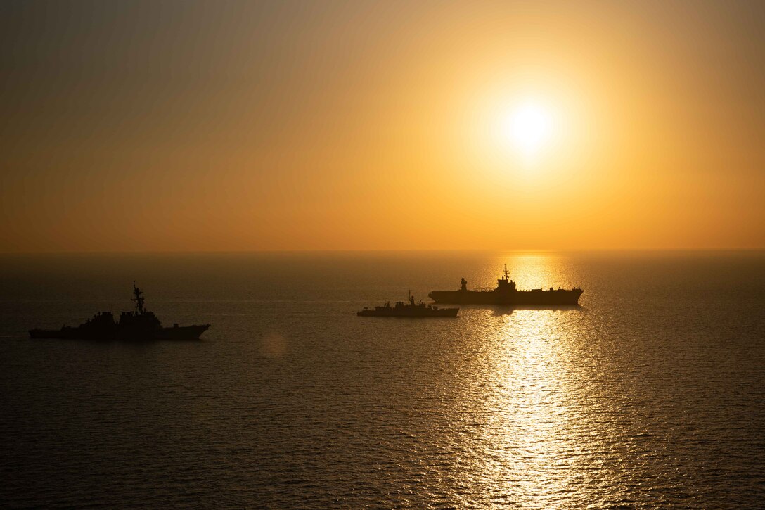 Three military ships sail near each other at twilight.