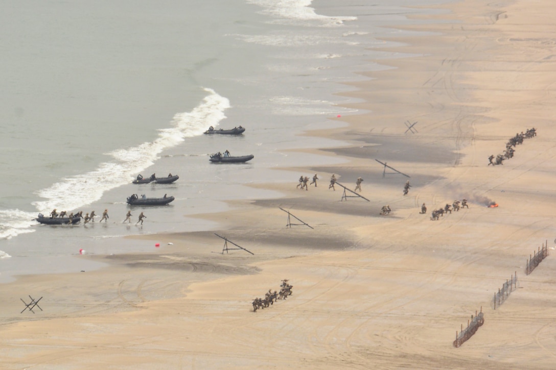 Troops in boats land on a beach with barricades set up.