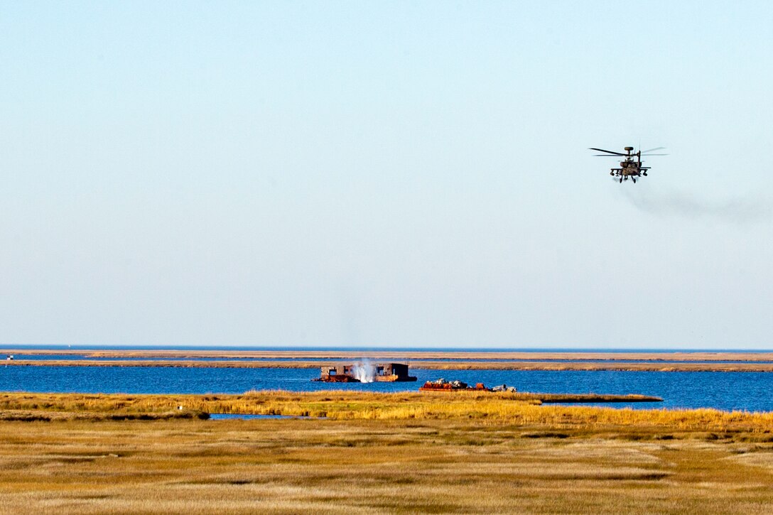 A rocket explodes to create a geyser in a marshy area while a helicopter hovers in the distance.