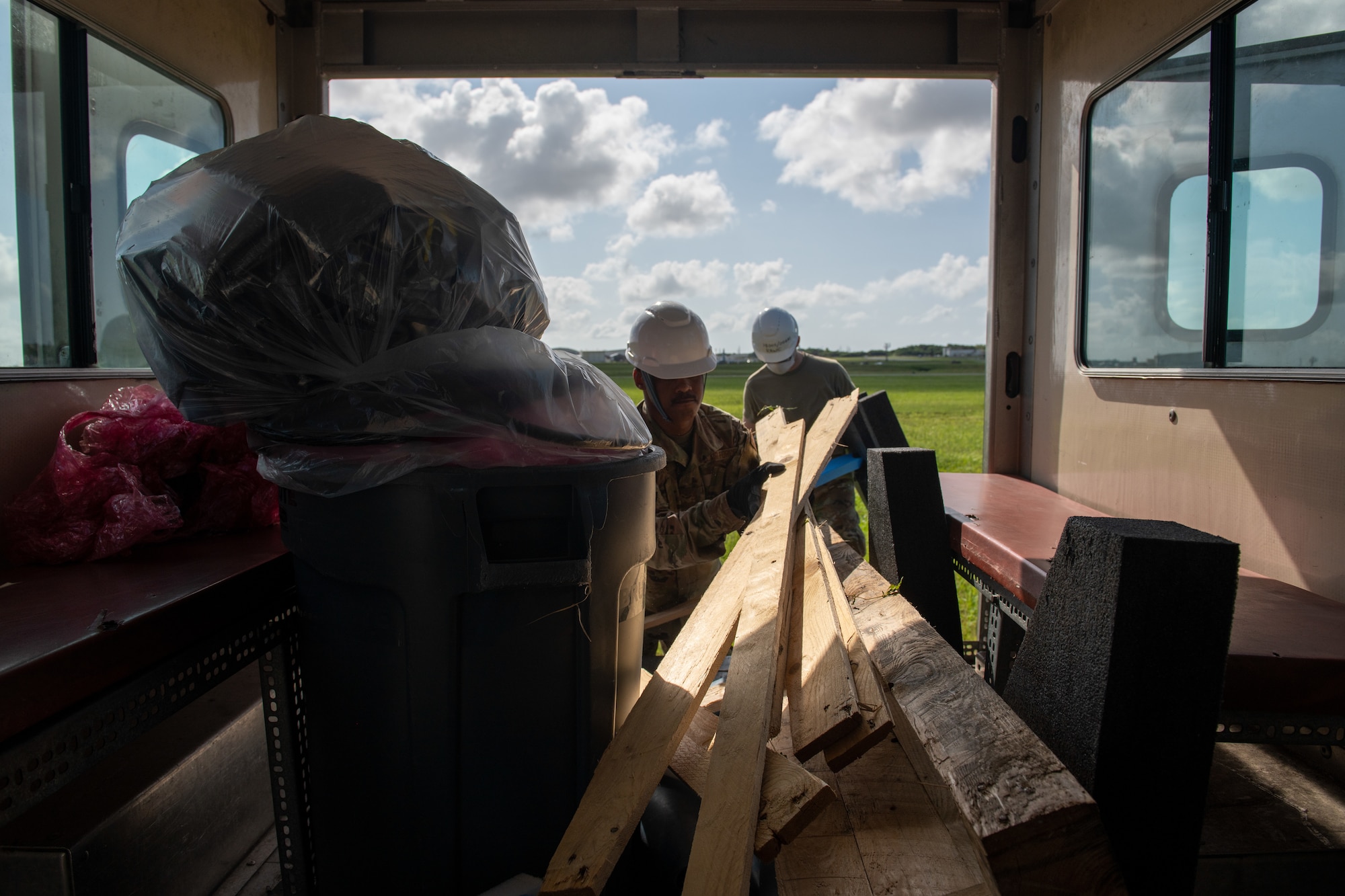 Two military members pull wooden planks out from the back of a truck