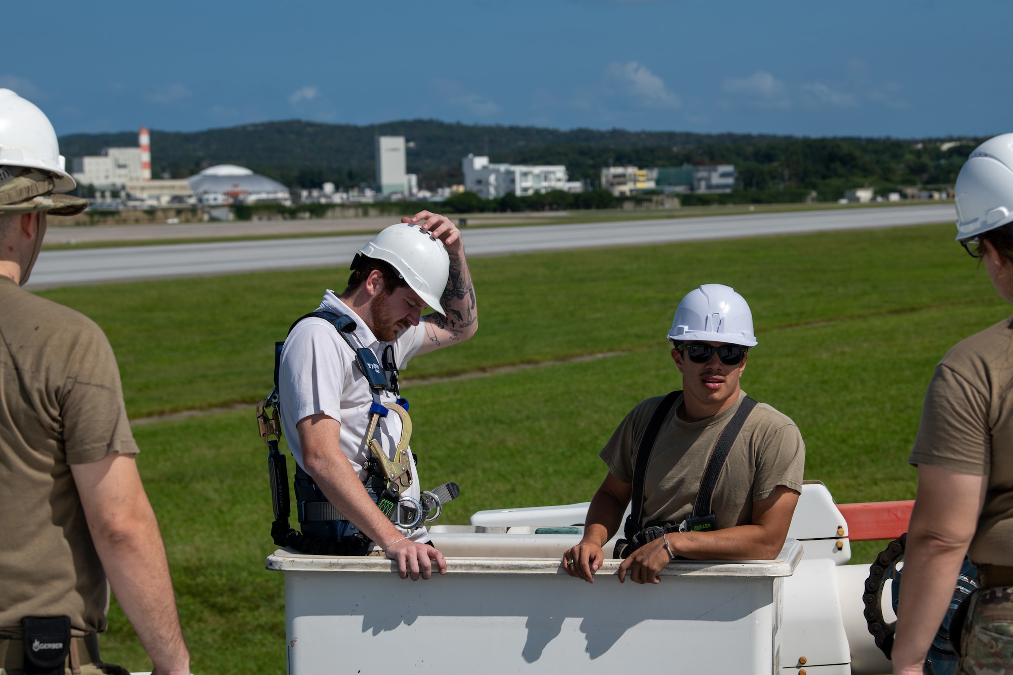 3 military members and a civilian in hard hats wait to work on the installation of an antenna