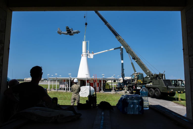 A plane flies overhead of a crane and military personnel