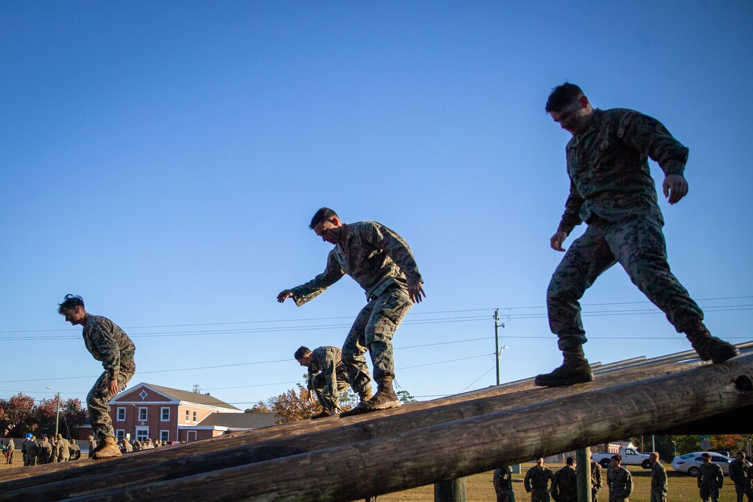 Four Marines walk across a wooden obstacle course.