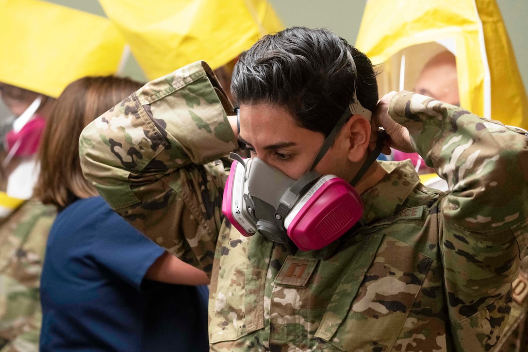 An airman puts on a respirator with the assistance of a nurse.