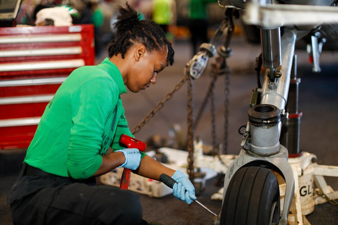 A sailor conducts maintenance on the tire of a helicopter aboard a ship.