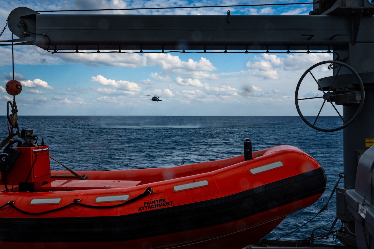 A helicopter flies over a body of water as seen from a nearby ship.
