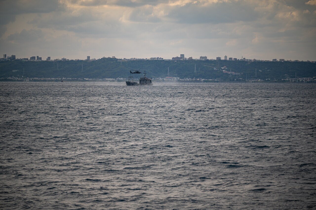 A helicopter hovers over a ship at sea.