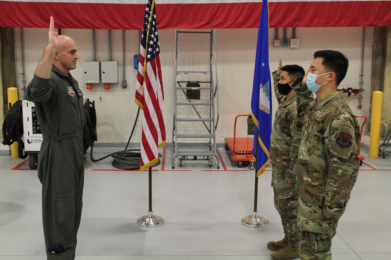 Two airmen raise their right hands while facing a third airman doing the same.