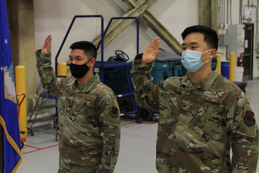Two airmen raise their right hands in a room.