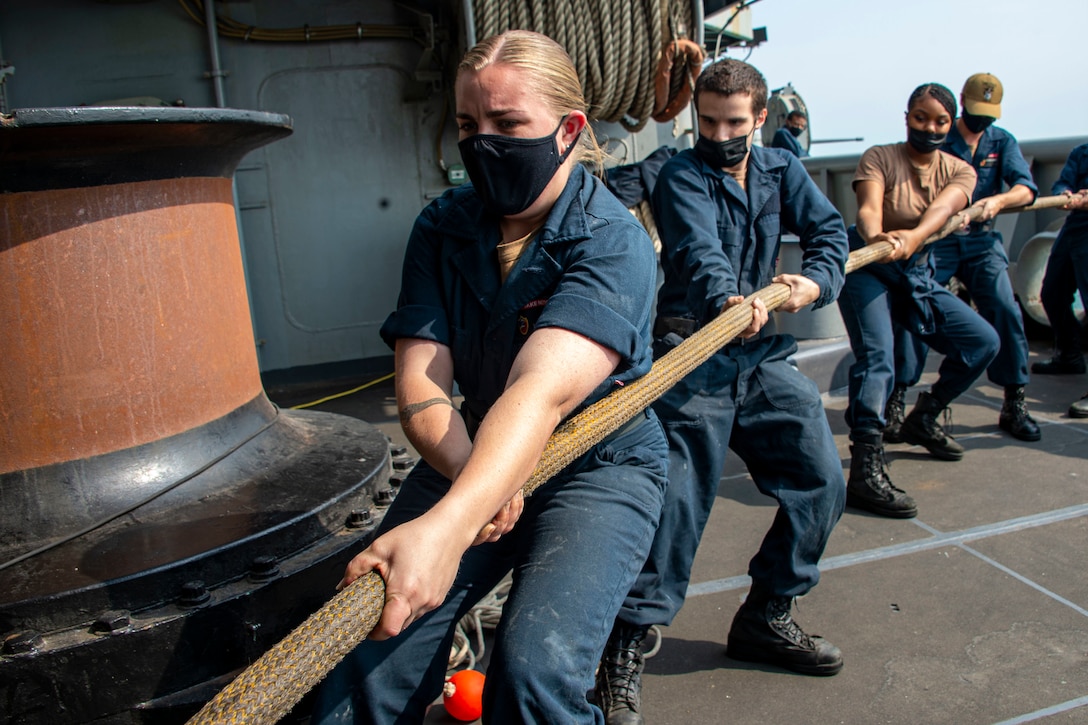 Sailors stand behind each other as they pull on a thick rope.