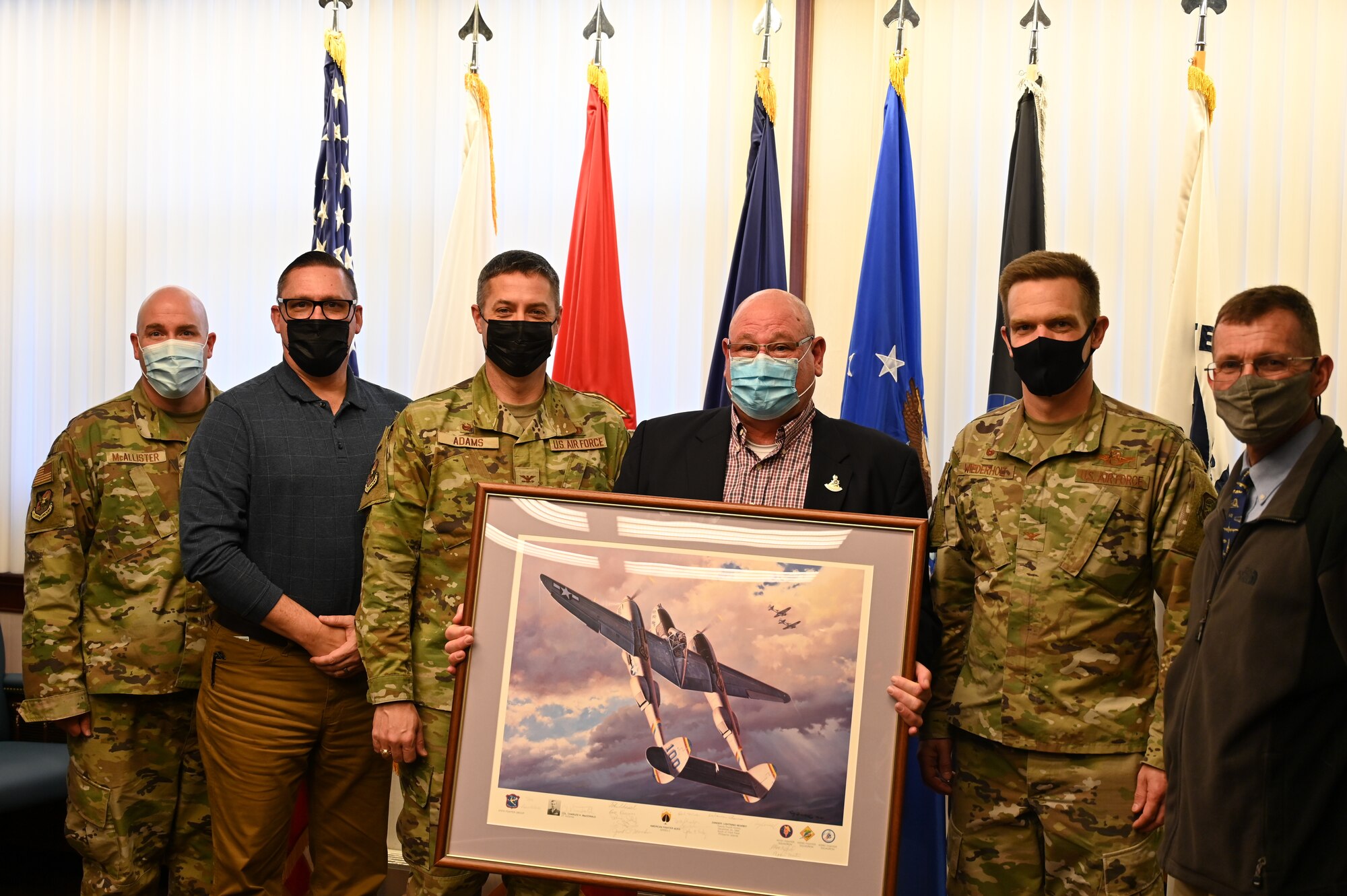 211129-F-BW403-1055 McGuire Air Force Base Senior Leadership pose with a donated P-38 lithograph at Joint Base McGuire-Dix-Lakehurst, N.J., Nov 29, 2021. The lithograph donated by Mr. David Tinker's came from his father who flew in the same Squadron as Major Tommy B. McGuire, Jr., the namesake of McGuire AFB. With his father's passing, he felt finding a new home for his father's limited edition lithograph was appropriate. The lithograph has the original signatures of thirteen members of the 475th Fighter Group including Colonel Charles MacDonald, who was McGuire's commanding officer in the Pacific during World War II.