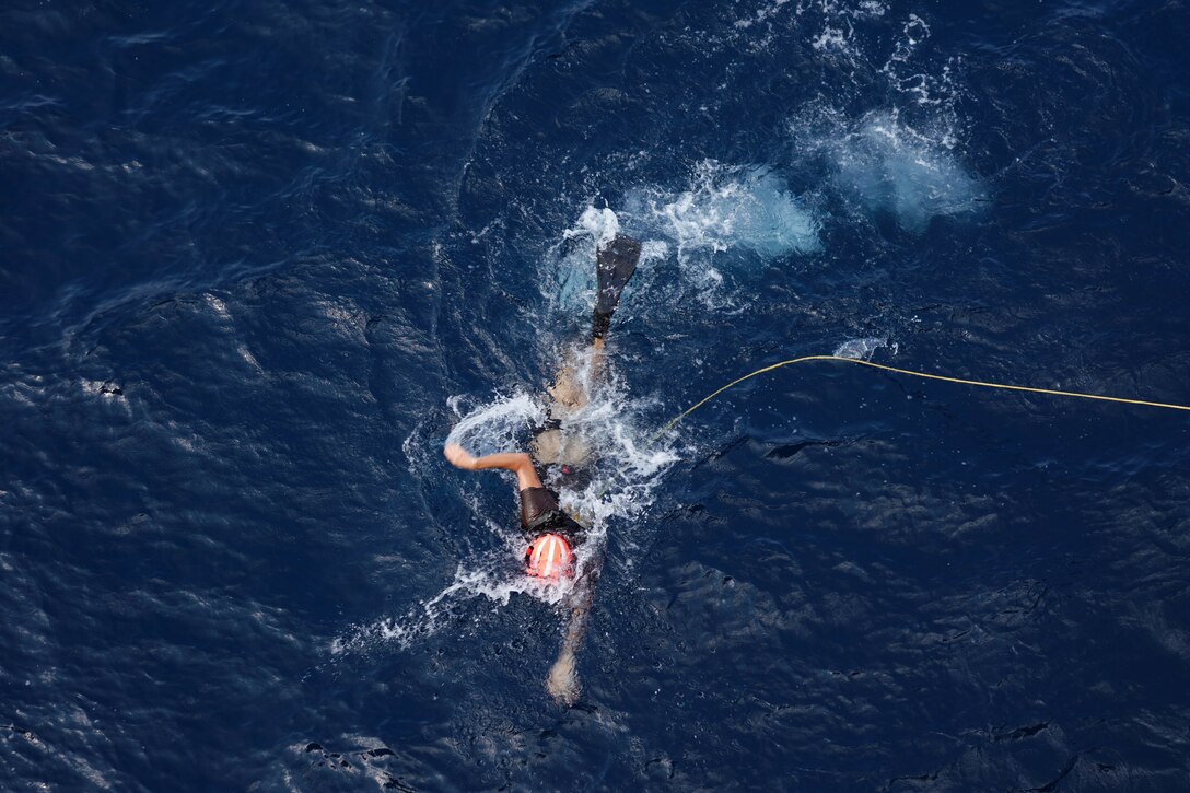 A sailor attached to a rope swims in dark blue water.