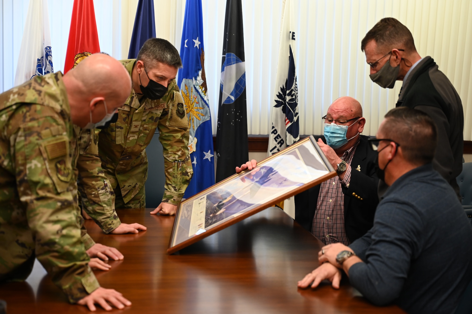 McGuire Air Force Base Senior Leadership inspect a donated P-38 lithograph at Joint Base McGuire-Dix-Lakehurst, N.J., Nov 29, 2021. The lithograph donated by Mr. David Tinker's came from his father who flew in the same Squadron as Major Tommy B. McGuire, Jr., the namesake of McGuire AFB. With his father's passing, he felt finding a new home for his father's limited edition lithograph was appropriate. The lithograph has the original signatures of thirteen members of the 475th Fighter Group including Colonel Charles MacDonald, who was McGuire's commanding officer in the Pacific during World War II.