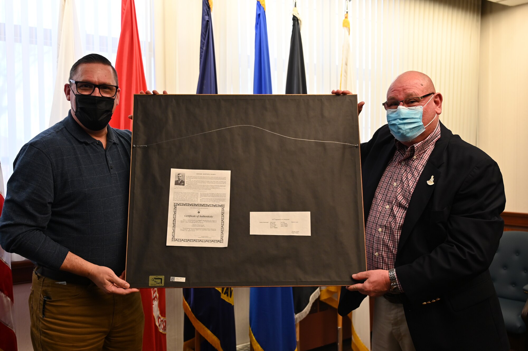 Mr. James Warrick, 87th Air Base Wing historian, and local New Jersey resident Mr. David Tinker pose with a donated P-38 lithograph at Joint Base McGuire-Dix-Lakehurst, N.J., Nov 29, 2021. The lithograph donated by Mr. David Tinker's came from his father who flew in the same Squadron as Major Tommy B. McGuire, Jr., the namesake of McGuire AFB. With his father's passing, he felt finding a new home for his father's limited edition lithograph was appropriate. The lithograph has the original signatures of thirteen members of the 475th Fighter Group including Colonel Charles MacDonald, who was McGuire's commanding officer in the Pacific during World War II.