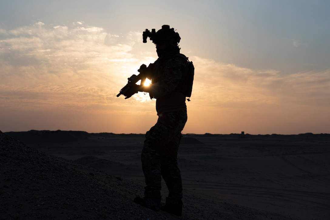 An airman stands and holds a weapon at twilight.