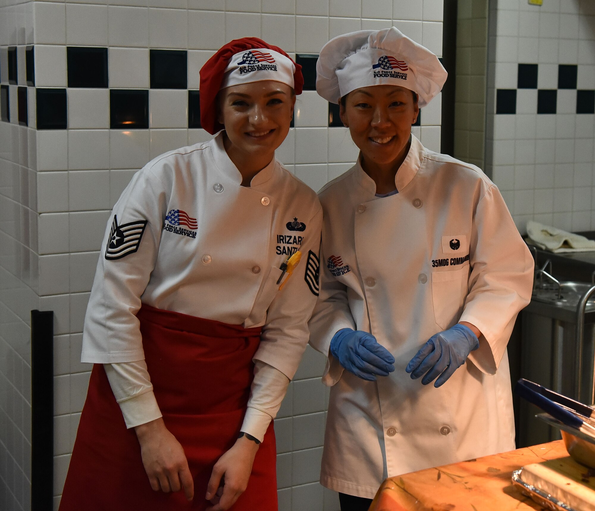 Two military members in cooking aprons pose for a picture.