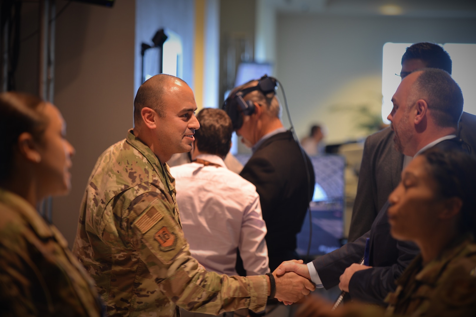 Airman shakes hands with a visitor at a booth.