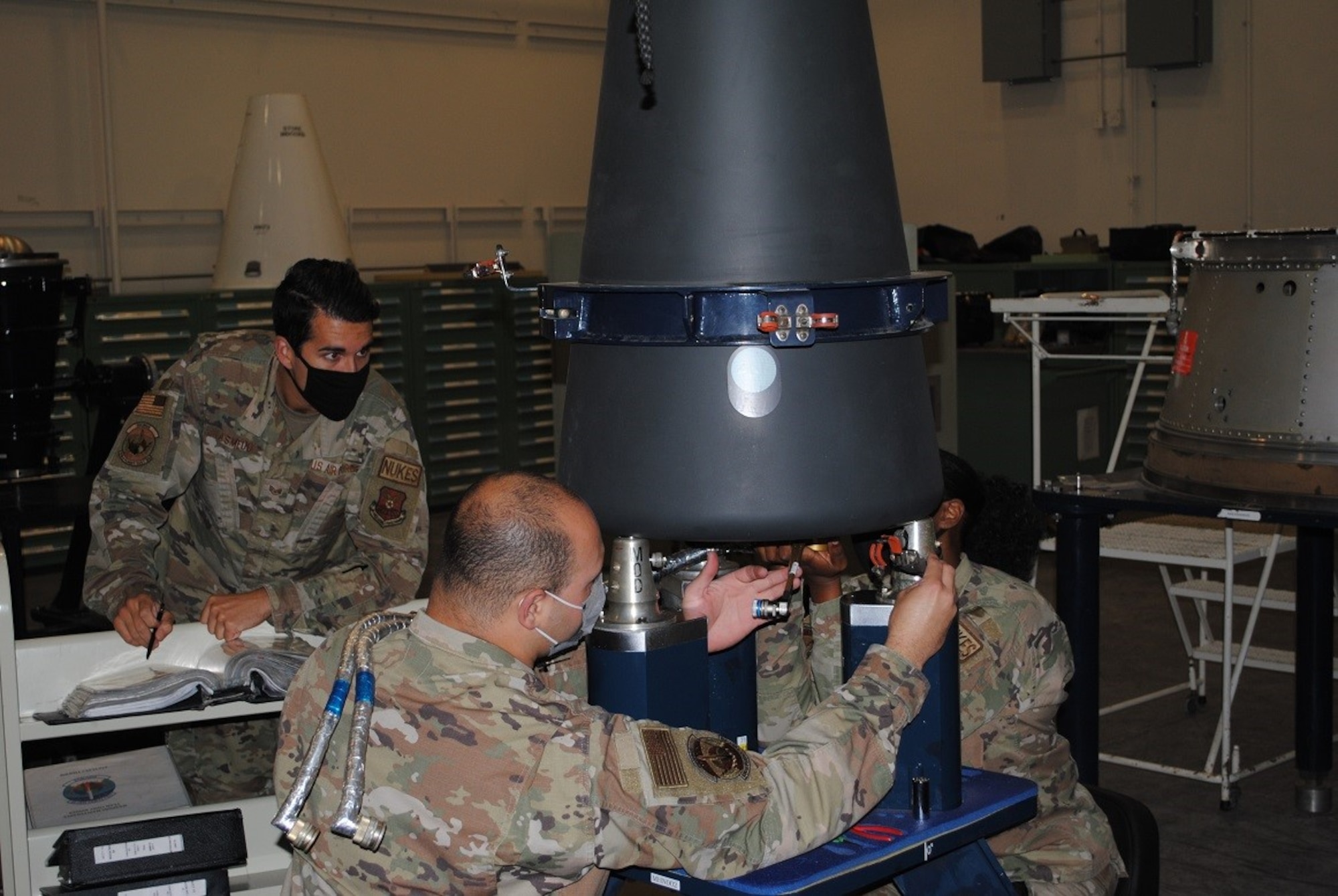 Three uniformed Airmen work on hardware.