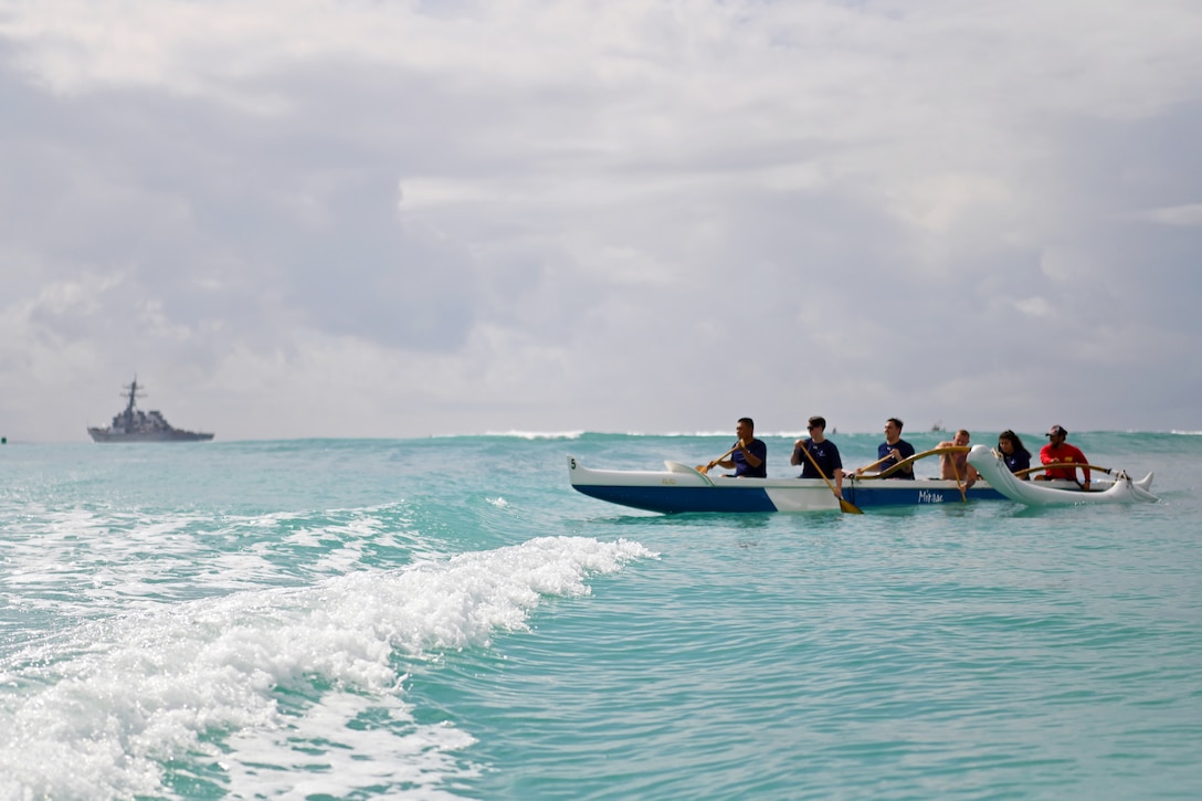 Wounded warriors paddle a boat in the ocean.