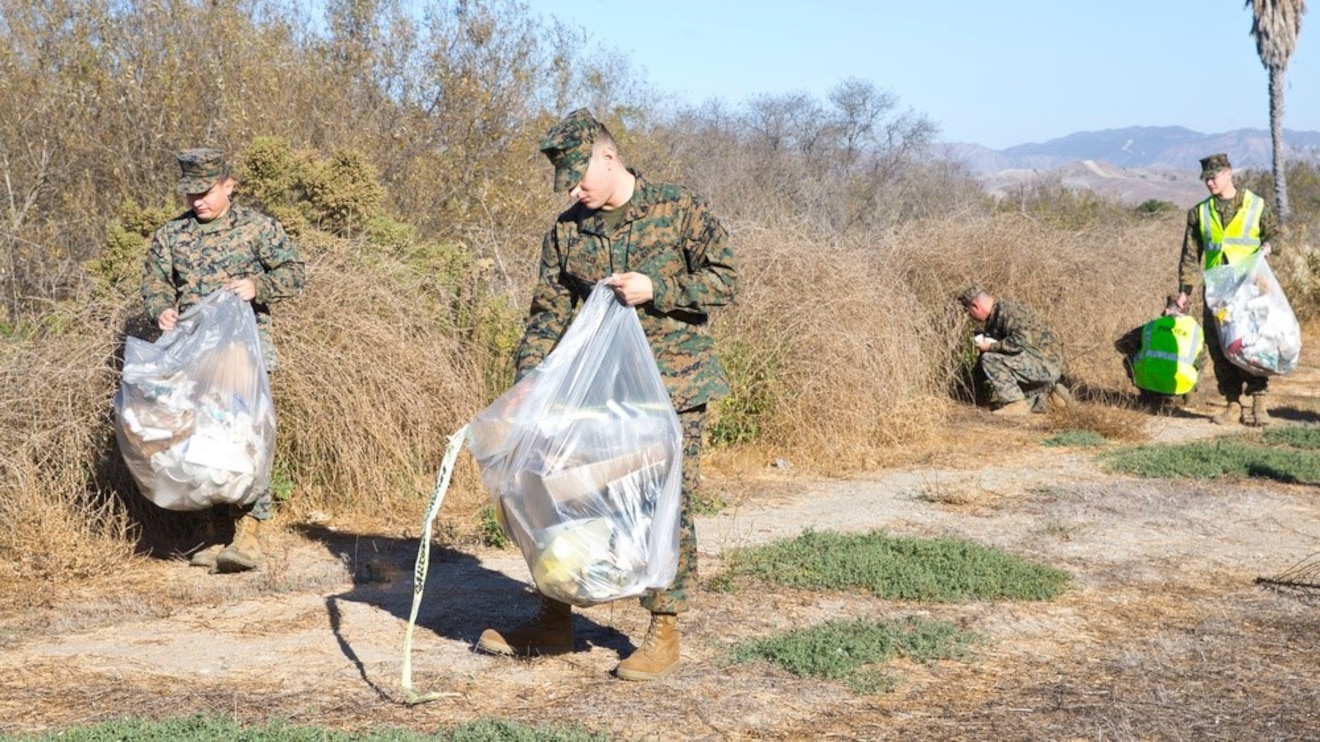 Marines in uniform collecting trash into bags outdoors.