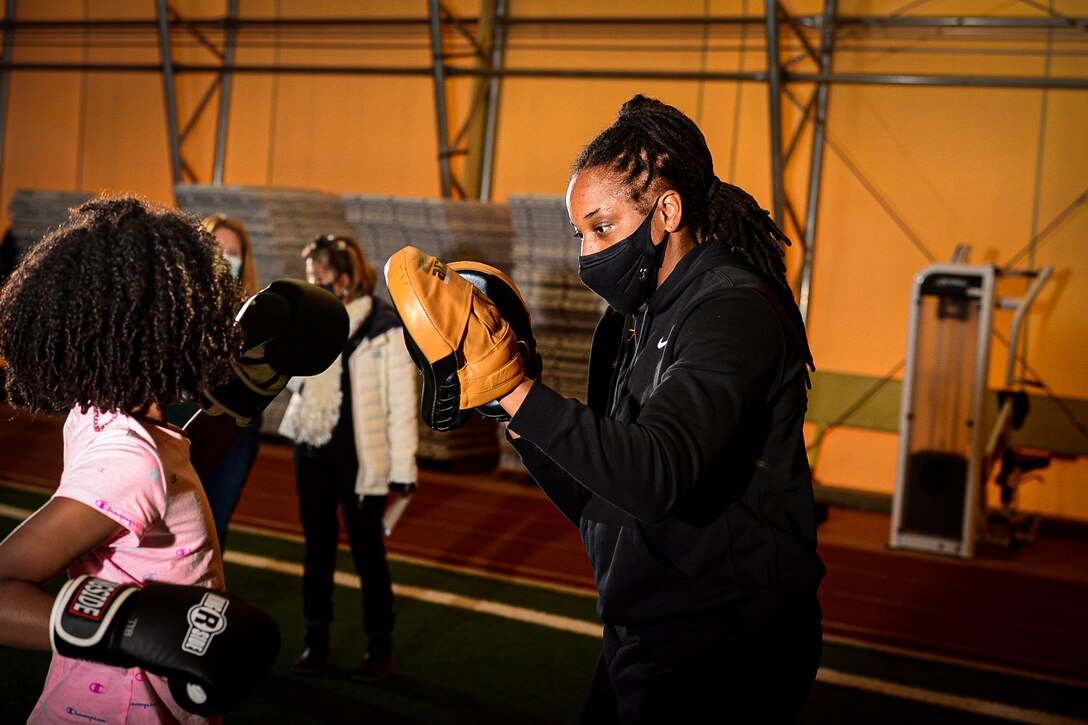 A soldier teaches a young girl how to box at a gym.