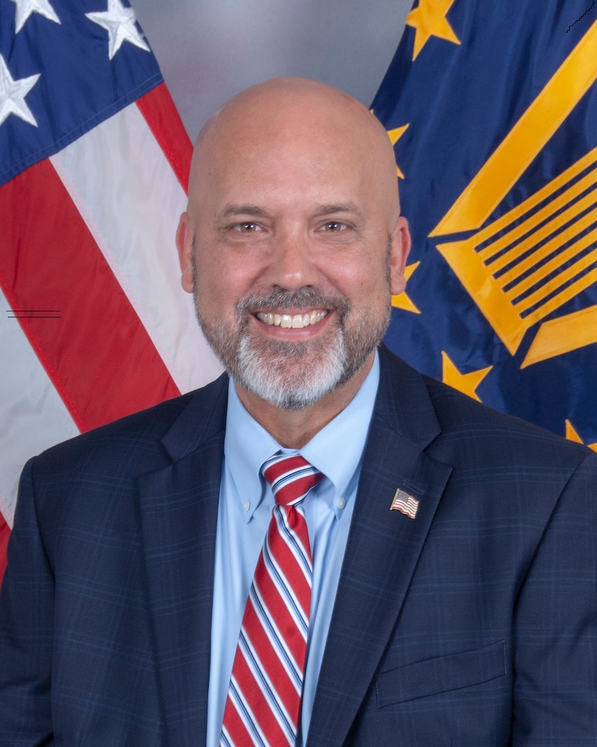 Man wears a dark suit with a blue shirt and red-striped tie