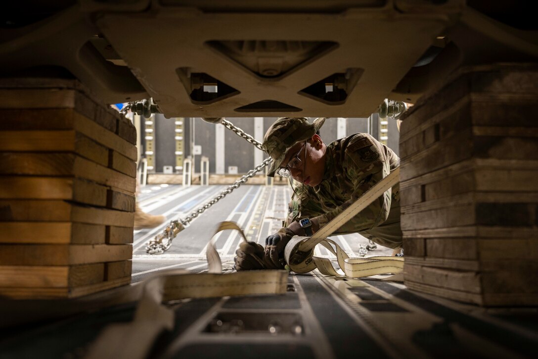 An airman secures a small vehicle to an aircraft.