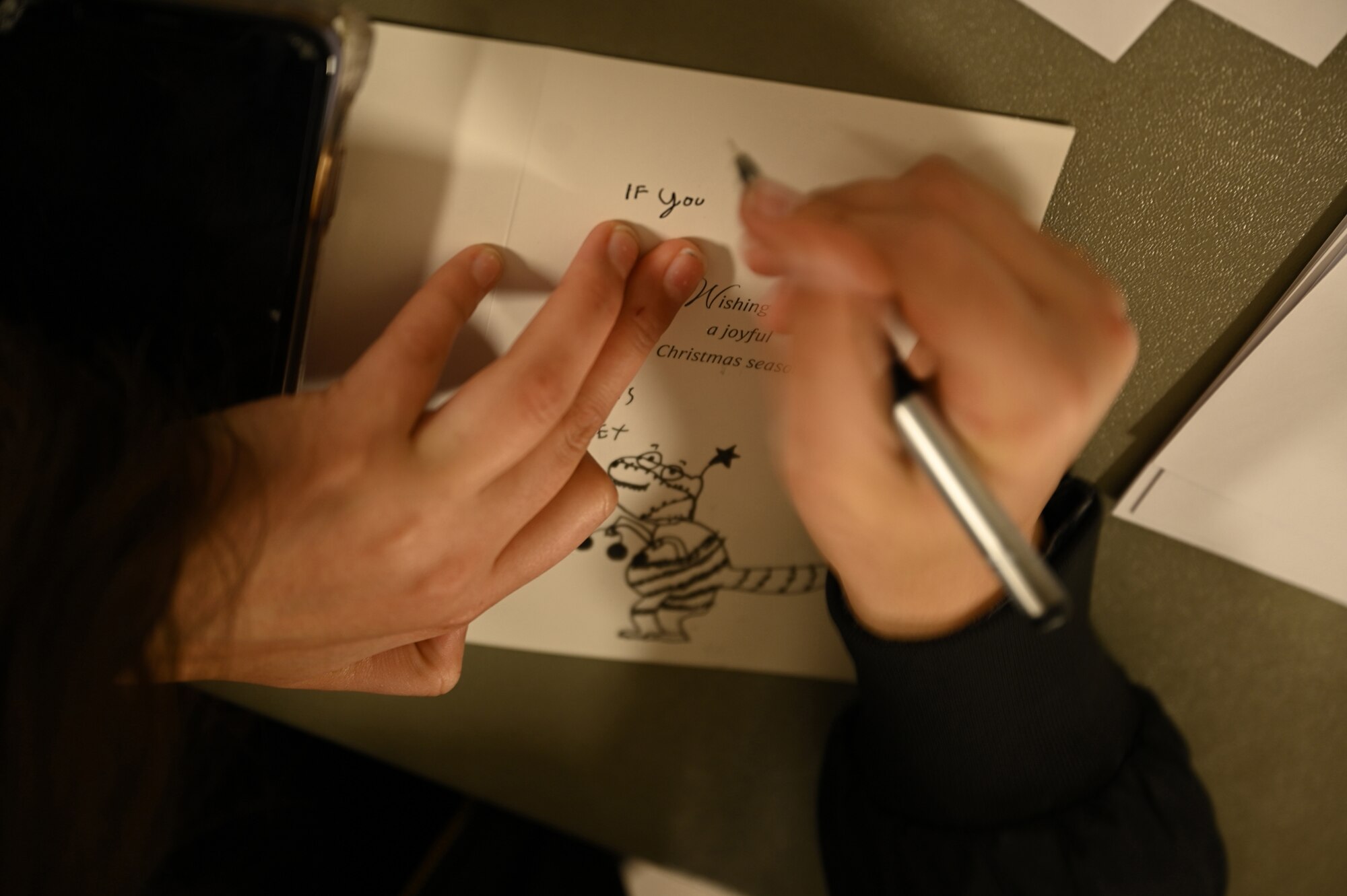 Haley Updike, a volunteer from the Office of Naval Intelligence, fills out a greeting card to share with veterans in local retirement homes during a holiday event in the chapel at Joint Base Anacostia-Bolling, Washington, D.C., Nov. 19, 2021. A group of more than 50 volunteers made up of U.S. Airmen, Sailors, and base and local community volunteers joined forces to support the chapel and first sergeant’s holiday charitable food drive. Volunteers packed bags with frozen chickens and turkeys, pasta, apple cider, fresh vegetables, and canned foods and distributed them to military families on base. (U.S. Air Force photo by Benjamin Matwey)