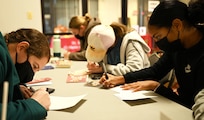 Volunteers from the Office of Naval Intelligence fill out greeting cards to share with veterans in local retirement homes during a holiday event in the chapel at Joint Base Anacostia-Bolling, Washington, D.C., Nov. 19, 2021. A group of more than 50 volunteers made up of U.S. Airmen, Sailors, and base and local community volunteers joined forces to support the chapel and first sergeant association holiday charitable food drive. Volunteers packed bags with frozen chickens and turkeys, pasta, apple cider, fresh vegetables, and canned foods and distributed them to military families on base. (U.S. Air Force photo by Benjamin Matwey)