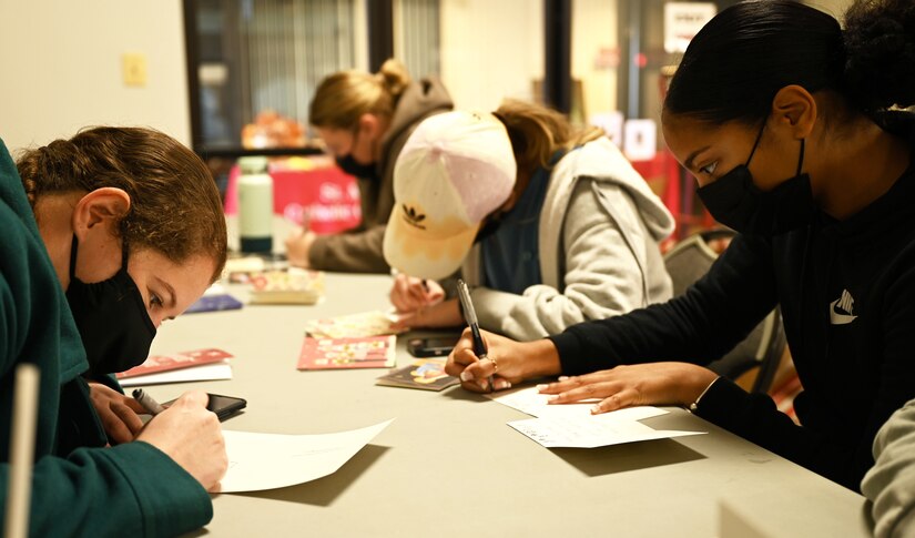Volunteers from the Office of Naval Intelligence fill out greeting cards to share with veterans in local retirement homes during a holiday event in the chapel at Joint Base Anacostia-Bolling, Washington, D.C., Nov. 19, 2021. A group of more than 50 volunteers made up of U.S. Airmen, Sailors, and base and local community volunteers joined forces to support the chapel and first sergeant association holiday charitable food drive. Volunteers packed bags with frozen chickens and turkeys, pasta, apple cider, fresh vegetables, and canned foods and distributed them to military families on base. (U.S. Air Force photo by Benjamin Matwey)