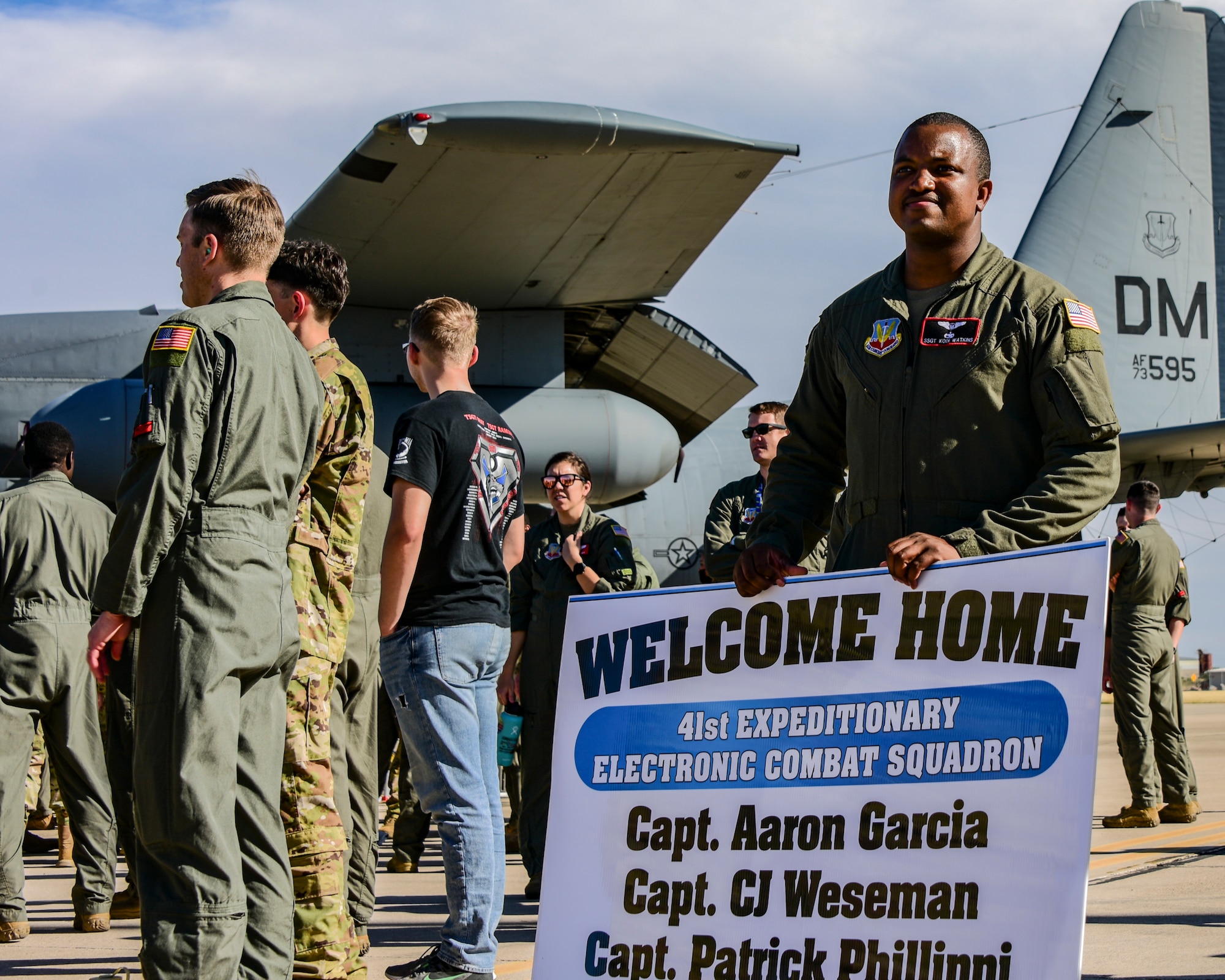 A photo of an Airman holding a welcome home sign.