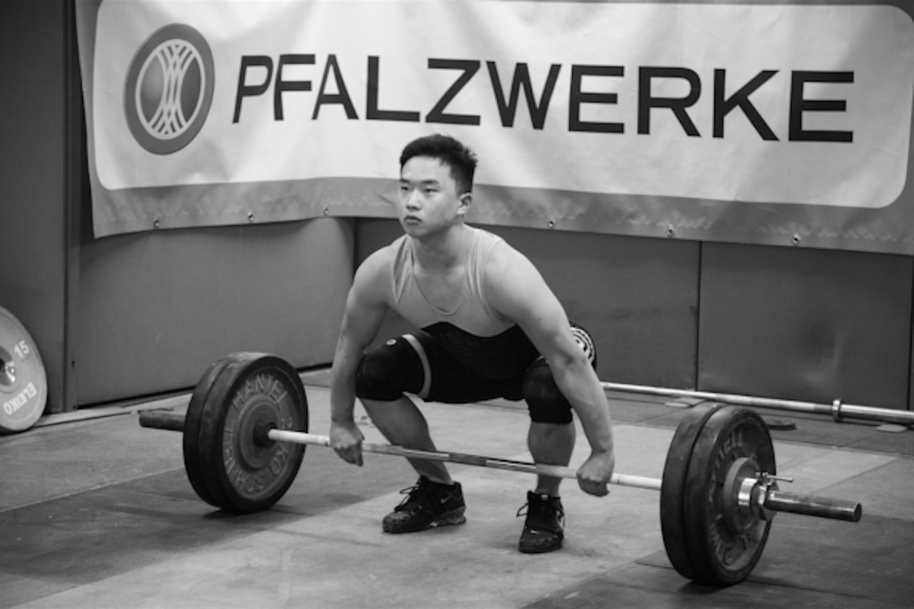 A person kneels and grasps a barbell with weights.