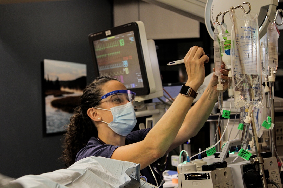 A sailor in scrubs adjusts the IV medication for a patient.