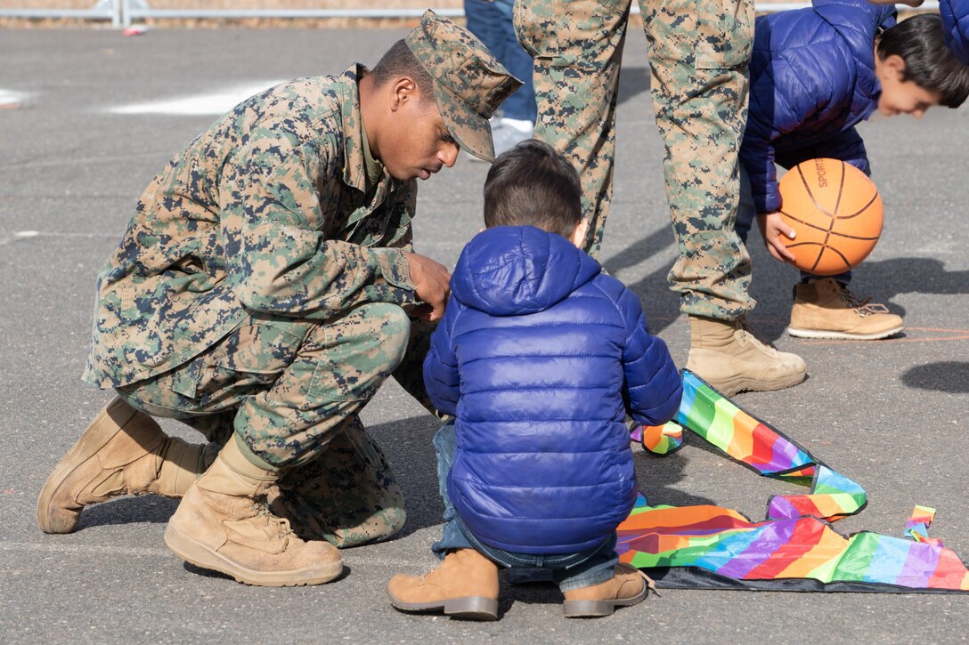 Marine kneels to help a child put together a kite.