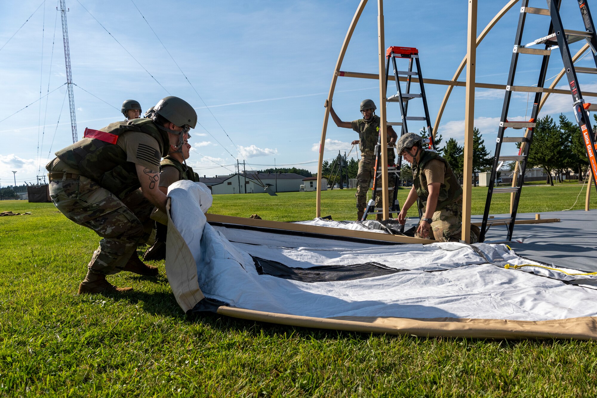 Airmen work together to lift tent door while setting up tent.