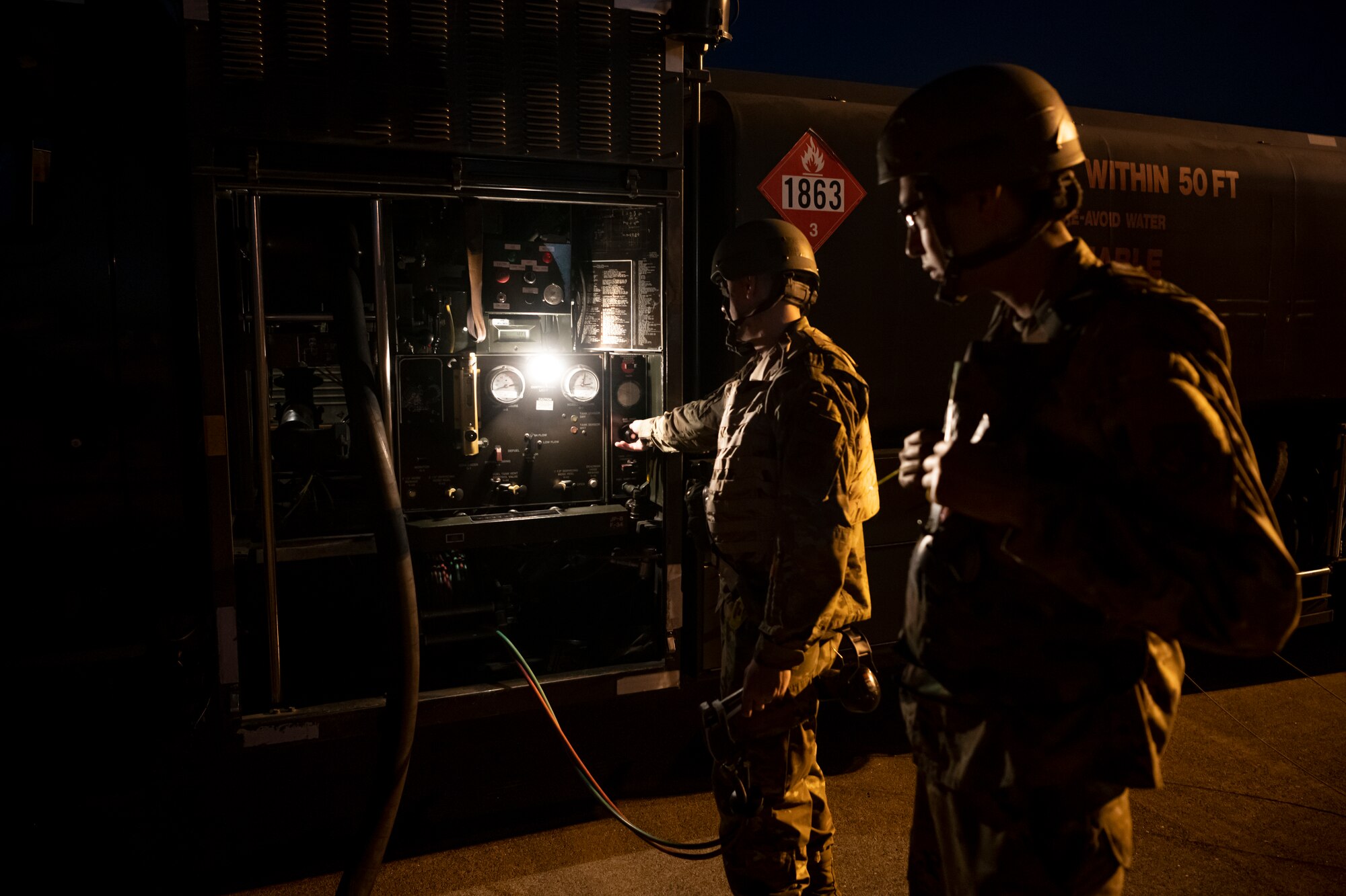 Airmen watching gauge on fuel truck while refueling aircraft at night.