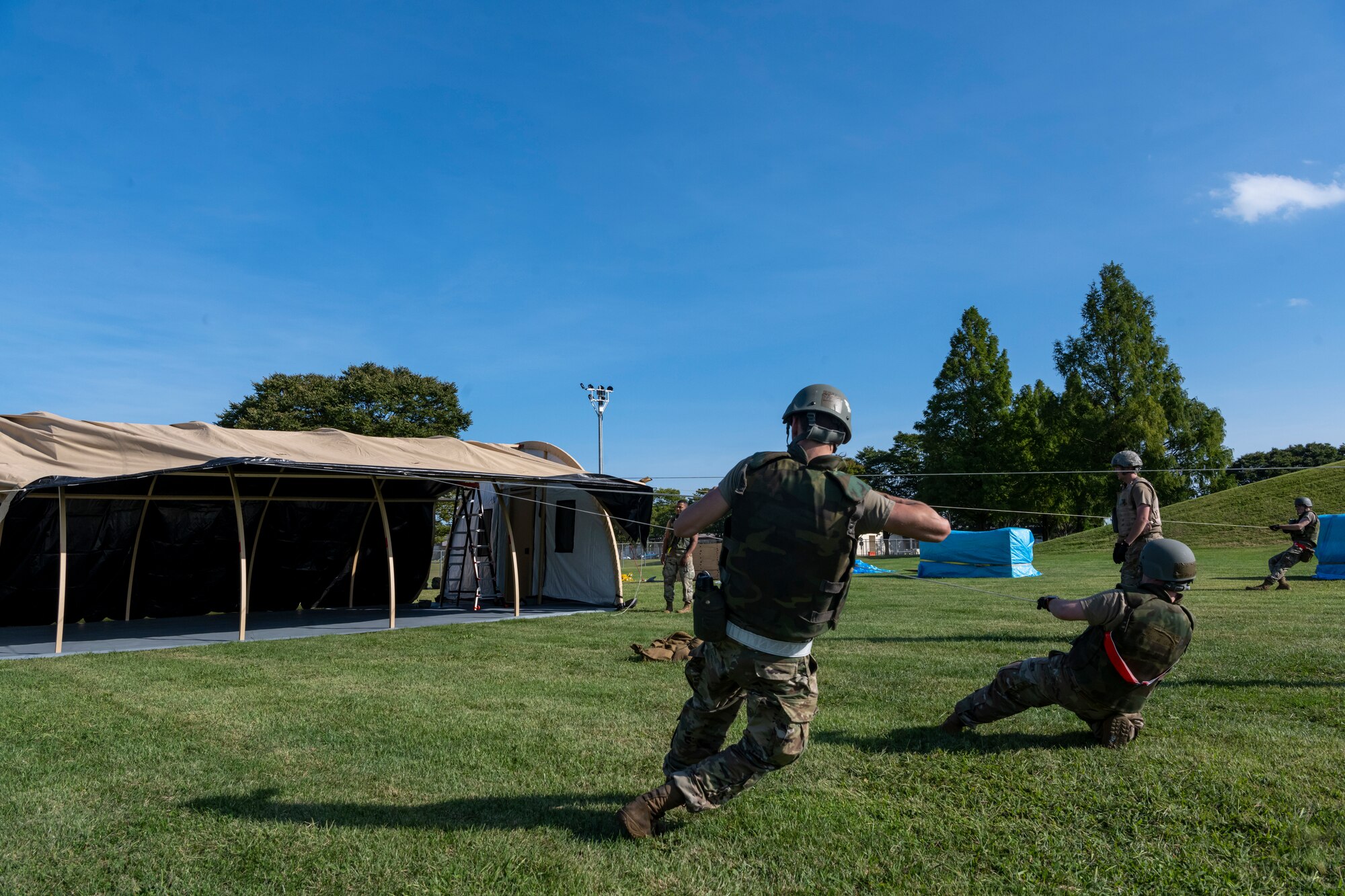 Airmen pulling strings attached to a cover to position tent covering over metal beams.