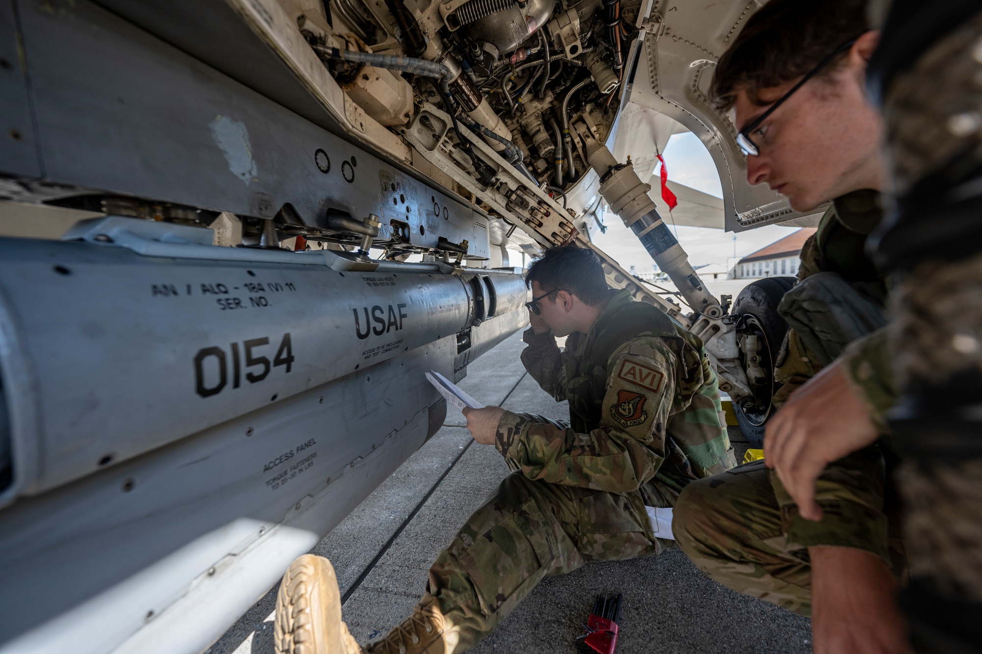 Airmen looking at part on the bottom of a fighter jet.