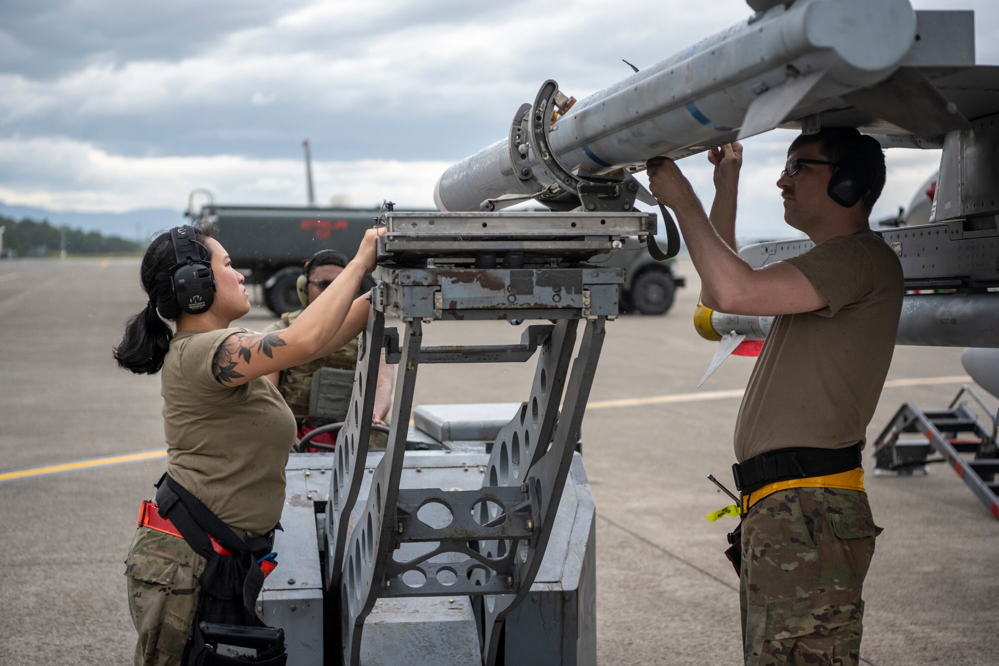 Airmen attaching a training ordnance onto an fighter jet on the flight line.