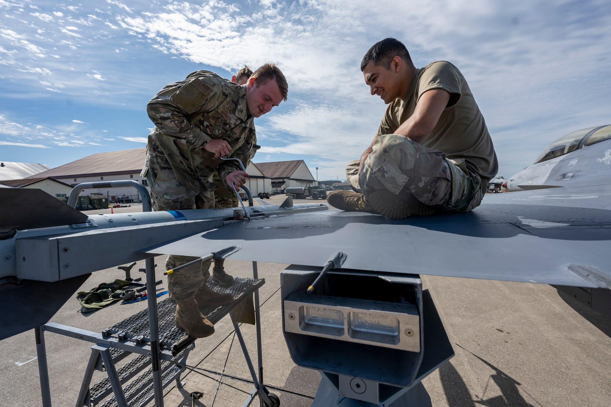 Airmen fasten a wingtip screw while standing on a jet on the flight line.