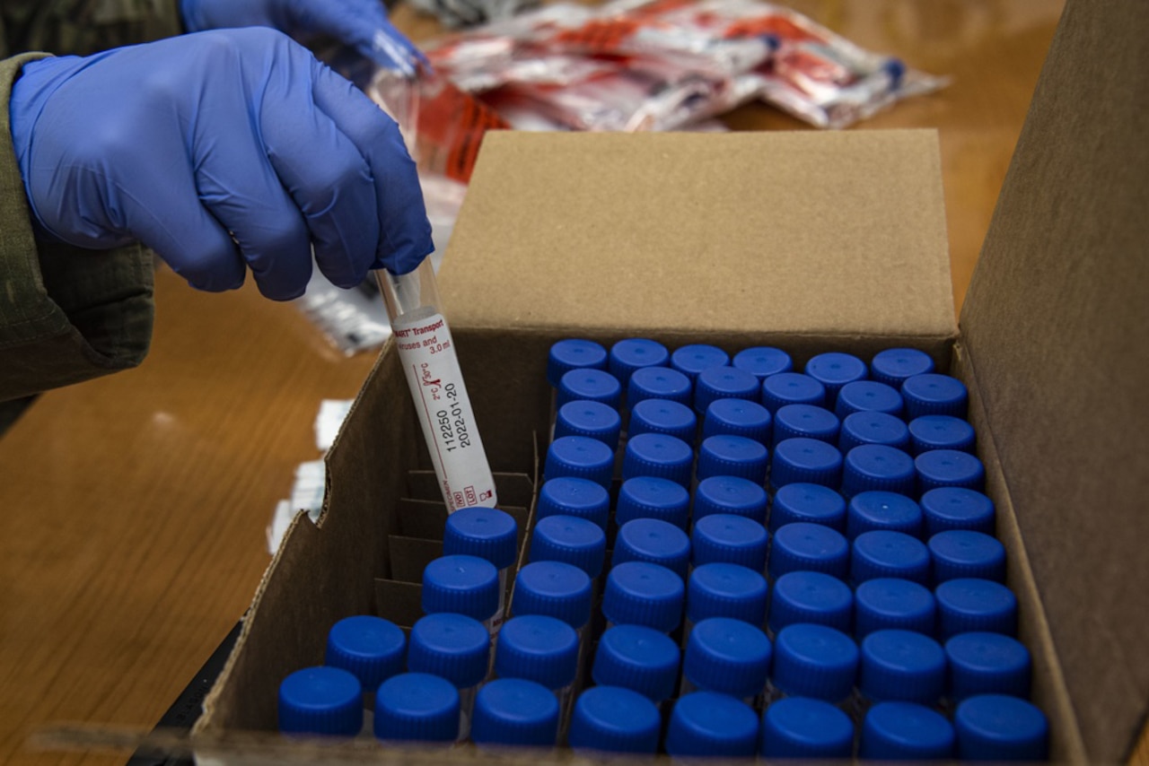 A service member puts a virus text kit into a box with other test kits.