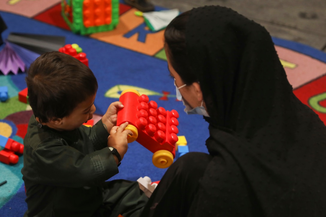 A woman watches as a young child plays with a toy car.