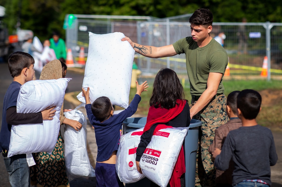 A Marine hands pillows to children outside.